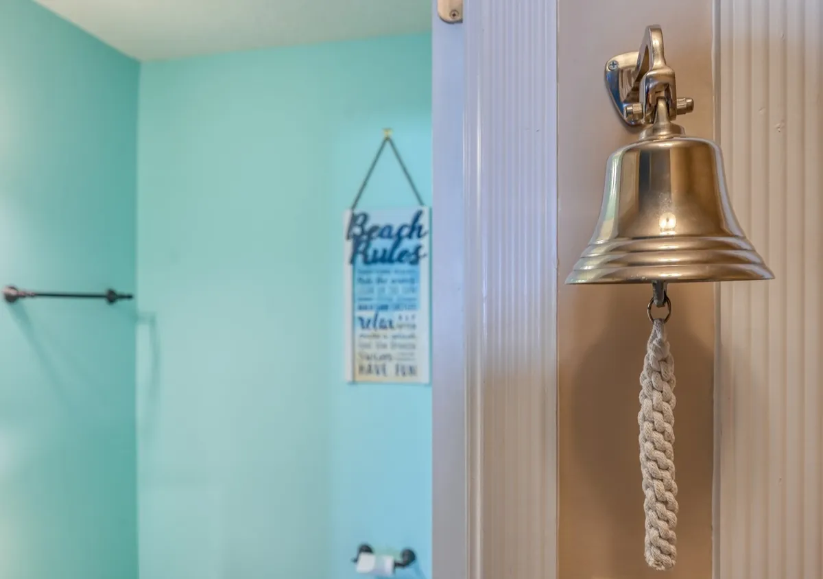 A lighthearted interior spot with a 'beach rules' sign and a bell, evoking the spirit of relaxed seaside living. The sign's playful guidance is surrounded by a breezy, informal atmosphere, suggesting the culture and rhythm of beach life.