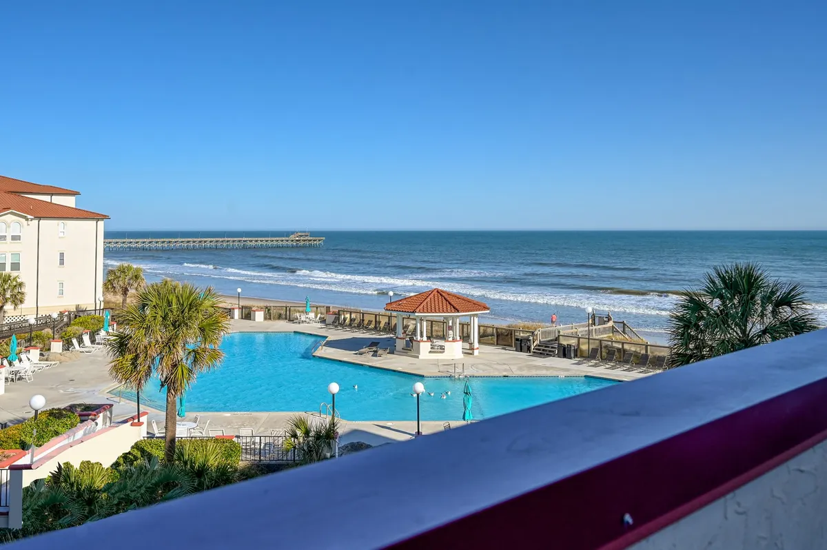 This image features a sweeping view of Villa Capriani's largest swimming pool, with palm trees swaying around the pool deck, a charming gazebo, and an expansive ocean view in the background. The nearby pier is visible, reinforcing the proximity to the beach and fishing activities.