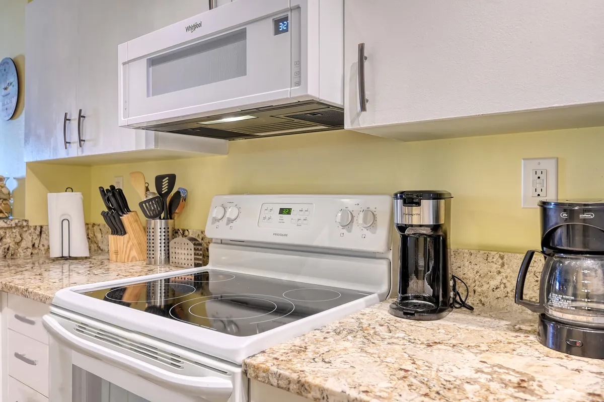 A cozy, well-equipped kitchen with granite countertops, stove, microwave, coffee maker, and utensils—perfect for preparing meals and gathering with loved ones. The space invites group cooking and dining, ideal for families and friends.