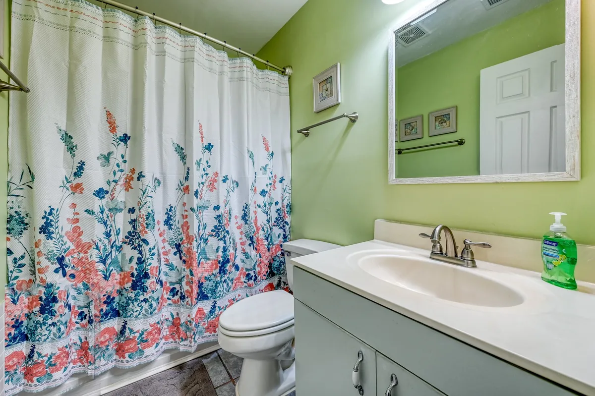 A serene bathroom scene with a floral shower curtain, a clean sink and faucet, and wall art that adds a personal, calming touch. The space feels private and inviting, echoing the idea of spa-inspired baths and personal pampering.