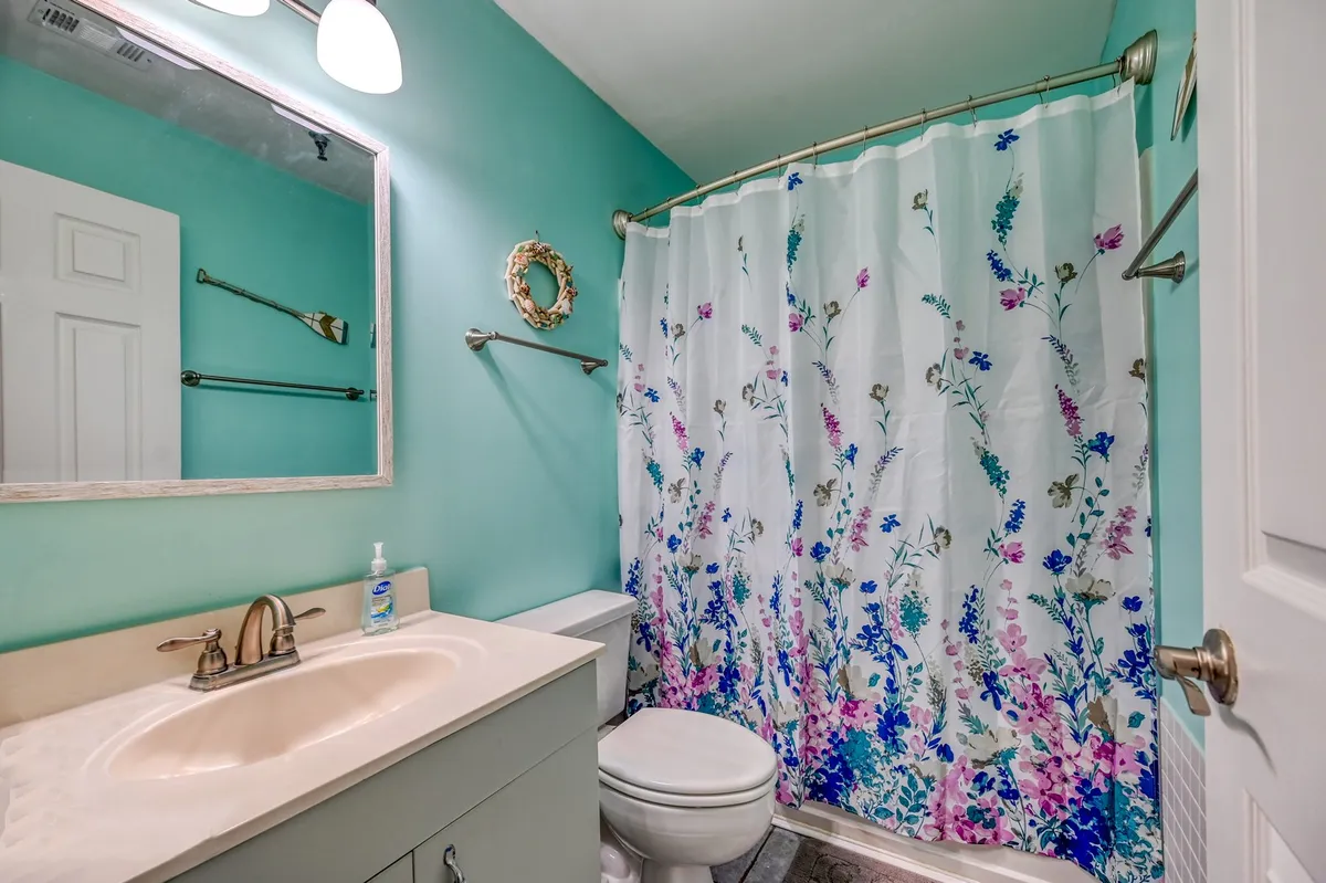 A serene ensuite bathroom with a vanity, sink, mirror, and shower curtain. The space feels fresh and clean, offering a peaceful spot for personal grooming and relaxation.