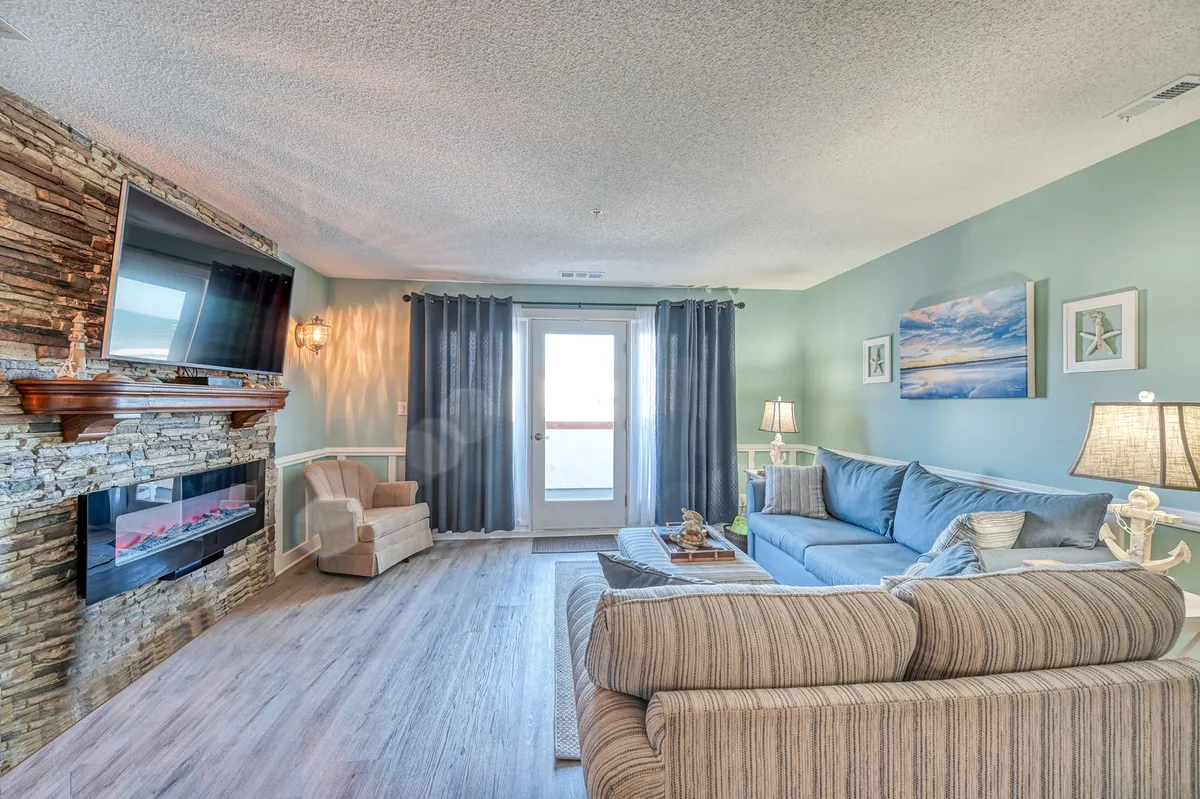 A cozy living room featuring a modern fireplace, a plush sofa, and large windows that let in abundant natural light. Decorative accents and soft furnishings create a tranquil, inviting space ideal for relaxation, reading, or quiet afternoons.