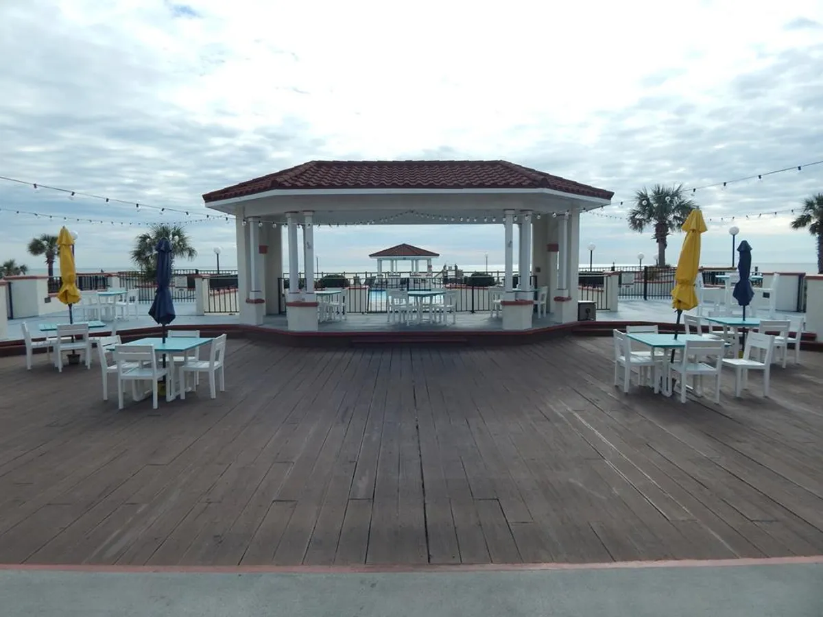 A tiled-roof pavilion with shaded seating areas and umbrellas overlooks the ocean, with ample space for al fresco dining or relaxing together. The ocean view and festive seating arrangements create an inviting atmosphere ideal for romantic dinners or sunset drinks.
