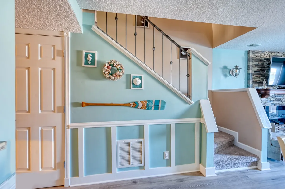 This image features a cheerful entryway with a staircase, a decorative oar, wreaths, and framed art, creating a welcoming first impression as guests arrive. The space is designed to greet family or friends warmly and hints at the multi-level layout of the condo.