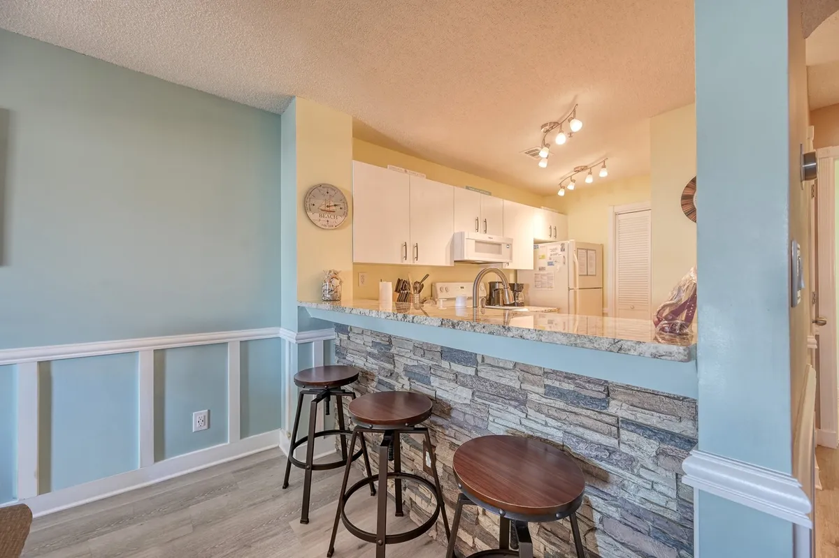This photo centers on a kitchen island with stools for three, a granite countertop, and white cabinets. The open seating area is ideal for casual breakfasts or chatting while prepping meals, echoing the kitchen’s connected, communal energy.