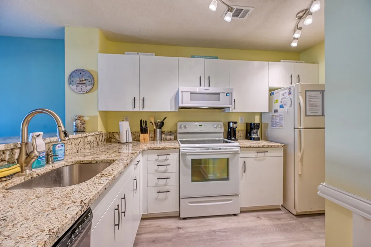 The image shows a kitchen with gleaming granite countertops, white cabinetry, and modern appliances. The setup is perfect for hosting, with enough space for people to gather and cook together, emphasizing the social aspect of the kitchen.